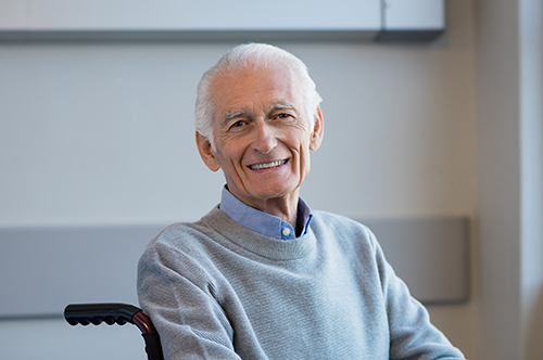 Elderly gentleman in gray sweater sitting in a wheelchair smiling